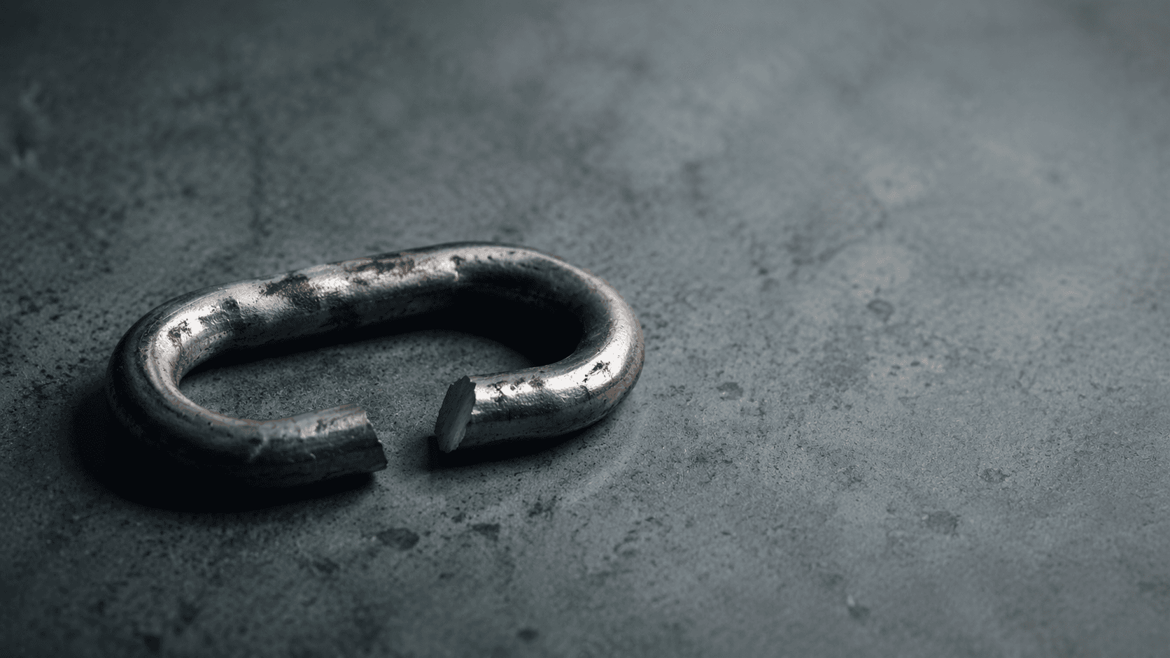 A single weathered steel chain link on a concrete surface, broken cleanly at one point — an editorial illustration of shared-fate risk in cloud infrastructure.